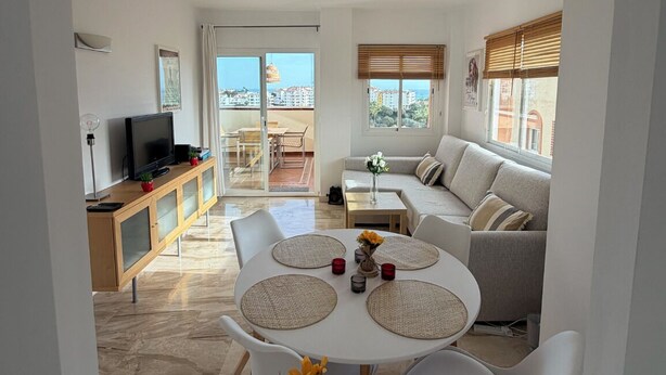 Una sala moderna con comedor, un sofá, un televisor y un balcón con vistas a edificios.