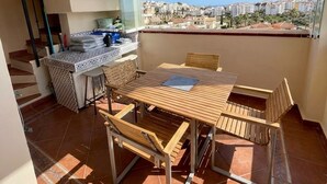 Un balcón con mesa y sillas de madera, una lámpara colgante y vistas de la ciudad.