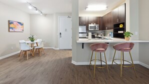 Et moderne køkken med mørke træskabe, et rustfrit stål køleskab og en mikrobølgeovn. Der er en hvid bordplade med barstole og et spisebord med stole.