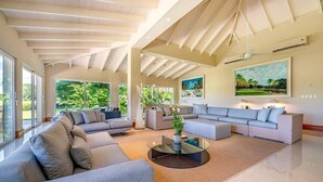Un salón espacioso con un sofá modular grande, una mesa de centro de vidrio y un cuadro de un paisaje tropical.