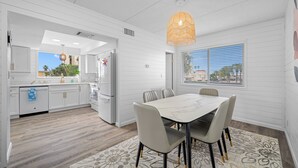 Une cuisine moderne avec des meubles blancs, un coin repas doté d’une table en marbre et une grande fenêtre avec des stores.
