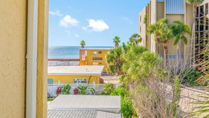Un bâtiment jaune avec vue sur la plage, des palmiers et une clôture blanche.