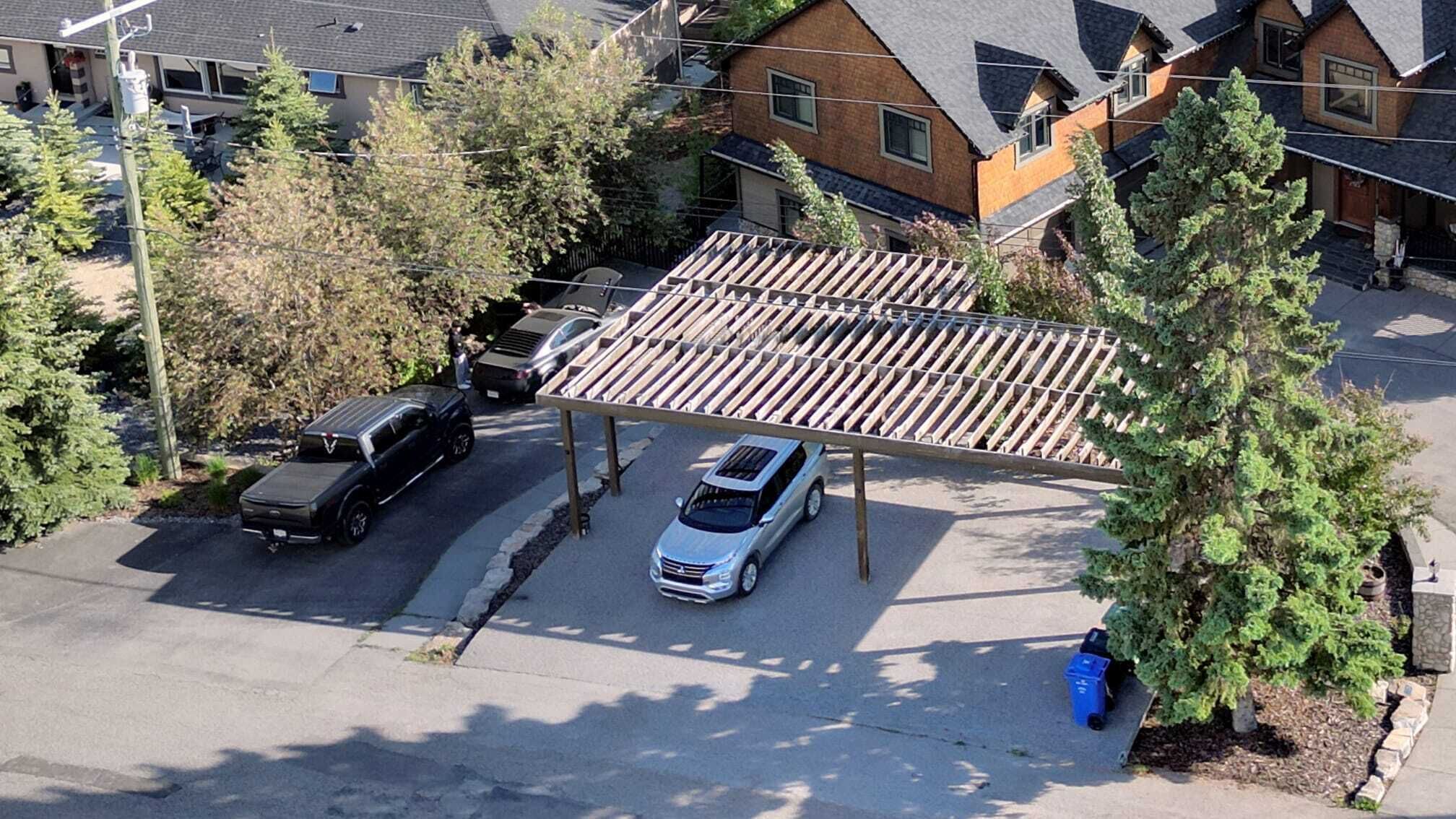 A parking area with a covered carport, two cars parked, and a tree nearby.