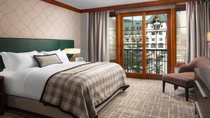 Habitación de hotel con una cama grande, una silla, un escritorio y un balcón con vistas a edificios.