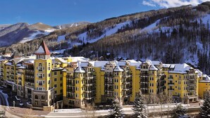 Un hotel amarillo de varios pisos con un patio central, rodeado de montañas nevadas y cielos despejados.