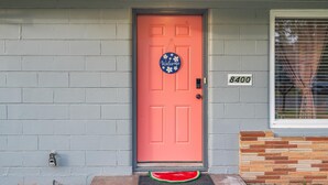 Una puerta rosa con un letrero de 'Welcome', un buzón y el número '8400'.