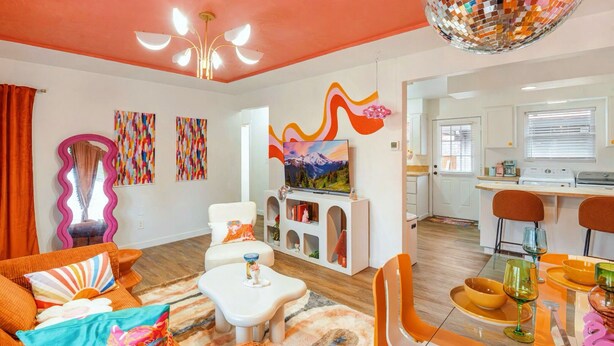 Una sala de estar moderna con un sofá, una mesa de centro y un televisor. Se observa una zona de cocina con una mesa de comedor y sillas.