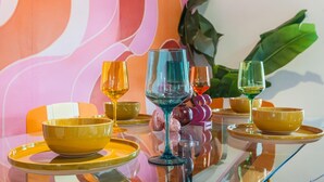 Una mesa de comedor con cuencos y vasos amarillos, frente a una pared vibrante y abstracta.
