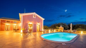 Una piscina con sillas de descanso y un pequeño edificio con luces, todo rodeado por un patio.