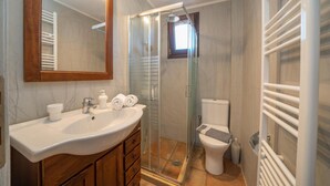 Un baño con ducha envuelta en vidrio, un lavamanos blanco sobre un mueble de madera y un inodoro con una toalla en el asiento.