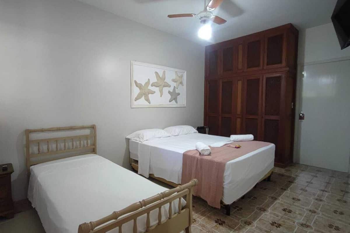 A bedroom with two single beds, a wooden nightstand with a lamp, a ceiling fan, and a large wardrobe.