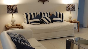 Uma sala de estar moderna com um sofá branco, um almofado listrado, uma mesa de centro de madeira e duas luminárias com cúpulas listradas.