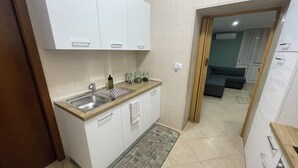 A modern kitchen with white cabinets, a stainless steel sink, and a wooden countertop. There is a small rug with a green pattern on the floor. - Green House Sea (Bisceglie)
