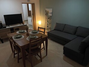 Una sala da pranzo con un tavolo di legno apparecchiato per quattro persone, una televisione e un divano nella zona living.