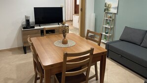 A modern living room with a wooden dining table, a flat-screen TV, a sofa, and a bookshelf. - Green House Sea (Bisceglie)