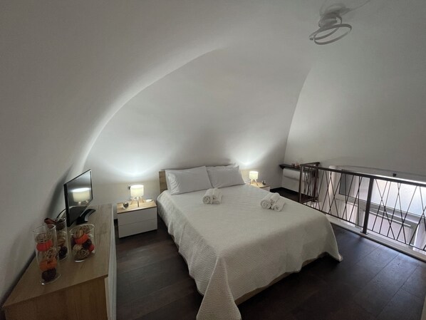 Una camera da letto con un letto, comodini, uno specchio e il parapetto del balcone.