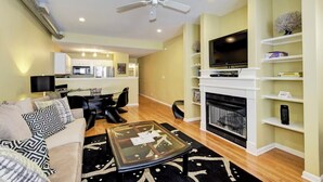 A living room with a sofa, coffee table, fireplace, TV, and kitchen in the background. - Charming Townhouse in Louisville – Explore the Urban Oasis! (Louisville)