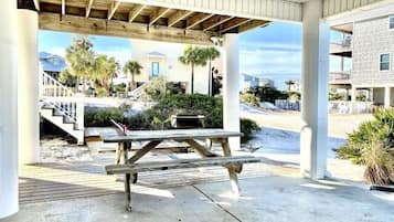 Un espacio cubierto al aire libre con una mesa de picnic, piso de concreto y vista a un barrio residencial con casas y palmeras.