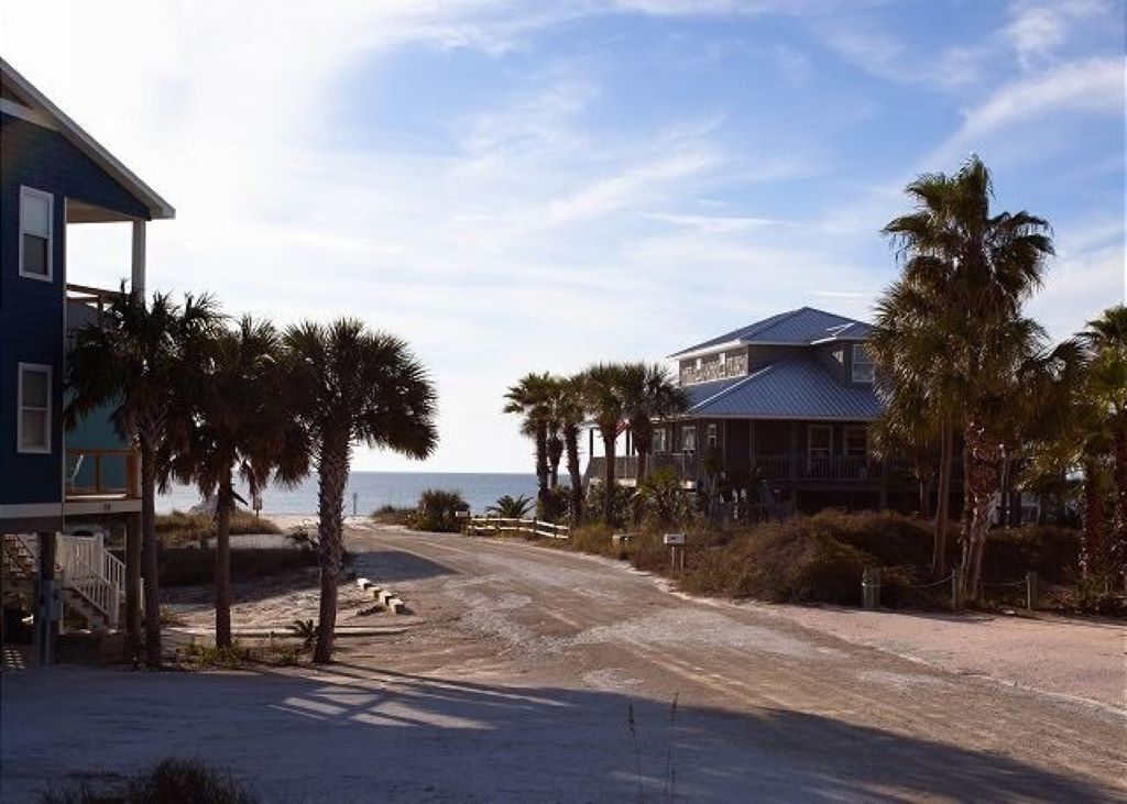 A beachfront property with a large house and a smaller building, surrounded by palm trees and a sandy beach.