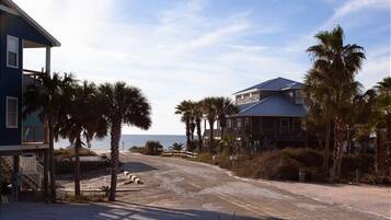 A beachfront property with a large house and a smaller building, surrounded by palm trees and a sandy beach.