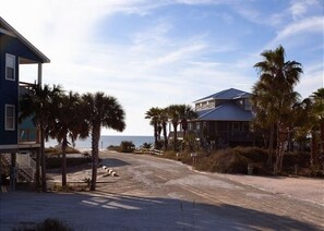 En fastighet vid stranden med ett stort hus och en mindre byggnad, omgiven av palmer och en sandstrand.