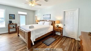 A bedroom with a wooden bed, a ceiling fan, a nightstand, a lamp, and a door. - Gulf View - 3 bed/3.5 bath Cape San Blas FL. Pet friendly! (Port St. Joe)