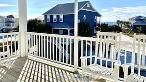 A covered porch with white railings and benches, overlooking a blue house with a dark roof and white trim, set against a clear sky. - Gulf View - 3 bed/3.5 bath Cape San Blas FL. Pet friendly! (Port St. Joe)