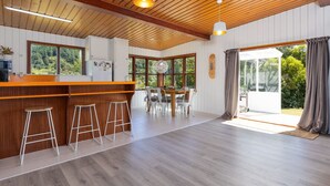 A spacious kitchen with wooden beams, a bar area with stools, and large windows offering views of the outdoors. - Waterfront Marlborough Sounds Retreat 10min drive from Picton (Whatamango Bay)