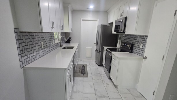 Una cocina moderna con armarios blancos, un refrigerador de acero inoxidable y un microondas.