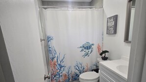Un baño con cortina de ducha con diseño de tortuga marina, un inodoro, un lavabo y un armario.