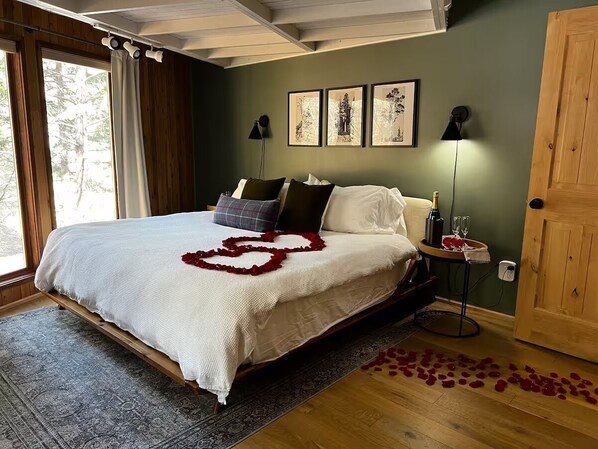 A bedroom with a large bed, a wooden floor, a rug, and a door. - THE Treehouse, Panoramic Views, Coffee Bar, KING Bed (Cascade-Chipita Park)