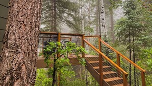 A wooden staircase leading up to a wooden deck surrounded by trees in a forested area. - THE Treehouse, Panoramic Views, Coffee Bar, KING Bed (Cascade-Chipita Park)