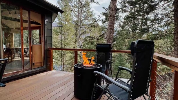 A wooden deck with a fire pit and two chairs, overlooking a forested area. - THE Treehouse, Panoramic Views, Coffee Bar, KING Bed (Cascade-Chipita Park)