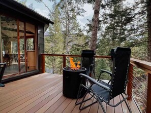A wooden deck with a fire pit and two chairs, overlooking a forested area. - THE Treehouse, Panoramic Views, Coffee Bar, KING Bed (Cascade-Chipita Park)