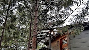A treehouse with a wooden staircase and a balcony, surrounded by tall pine trees. - THE Treehouse, Panoramic Views, Coffee Bar, KING Bed (Cascade-Chipita Park)
