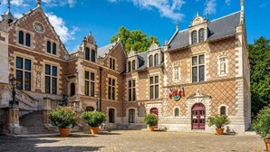 A historic building with a courtyard, featuring a central staircase, multiple windows, and flags. - The suite - Cosy hotel room ambience. Pets welcome! (Orléans)