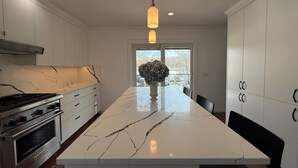 Una cocina moderna con una isla grande, armarios blancos, una estufa a gas y una lámpara colgante.