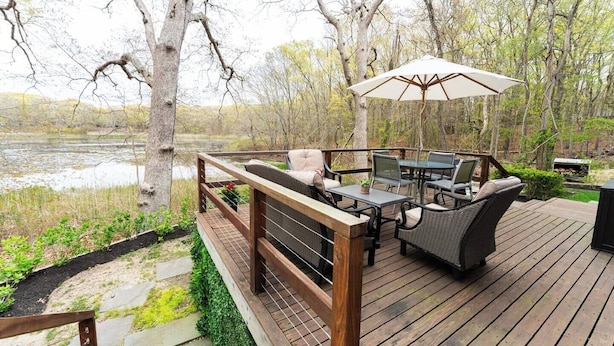 Una terraza de madera con mobiliario exterior, incluyendo una mesa y sillas, y un gran paraguas.