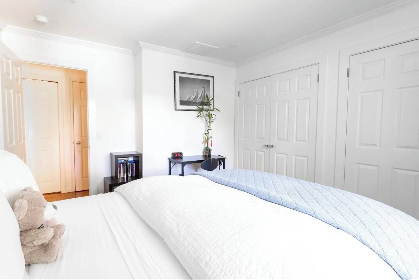 A bedroom with a large bed, a bedside table with books, a clock, and a framed picture on the wall.