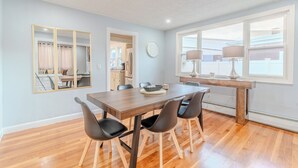 Un comedor con mesa de madera, sillas negras y una ventana con cortinas.