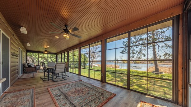 A spacious room with large windows, a ceiling fan, and a view of a lake.