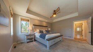 A bedroom with a bed, nightstands, a ceiling fan, a window, and a door leading to a bathroom.