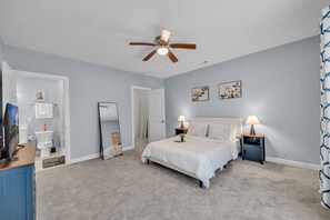 Une chambre à coucher comprenant un lit, des tables de chevet, un ventilateur de plafond, ainsi qu’une salle de bain avec des toilettes et un lavabo.