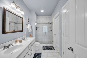 Une salle de bain moderne avec un grand miroir, deux lavabos, des toilettes et une douche à l’italienne.