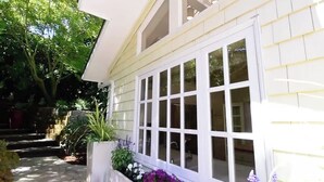 A house with a large window, a garden with flowers, and a pathway leading to the house. - Central Marin Living - 3 Bedroom House in Corte Madera (Corte Madera)