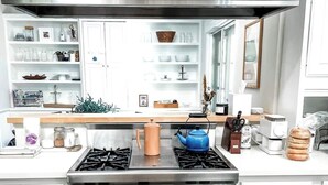 A modern kitchen with white cabinetry, a stainless steel range hood, a gas stove, and a blue kettle. - Central Marin Living - 3 Bedroom House in Corte Madera (Corte Madera)