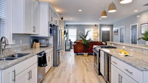 Una cocina moderna con armarios blancos, encimeras de granito y electrodomésticos de acero inoxidable, con una isla central.
