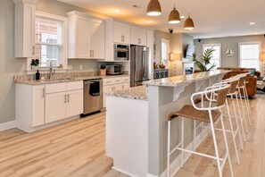 Une cuisine moderne avec des meubles blancs, des appareils en acier inoxydable et un coin bar agrémenté de chaises en osier.