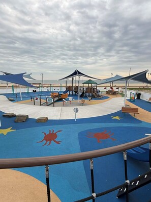 A playground with colorful play structures, a seating area, and a view of the beach.
