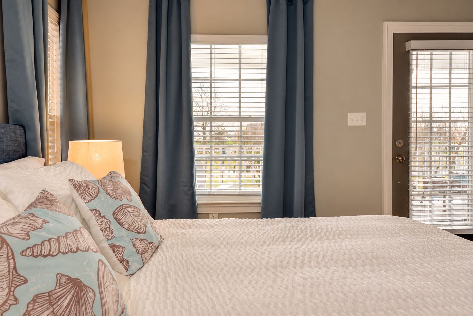 Une chambre à coucher avec un lit, des rideaux, une fenêtre avec des stores et une porte.